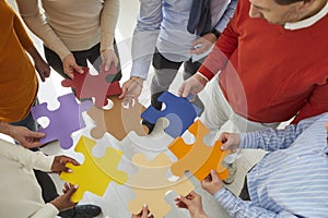 Team of business people joining colorful jigsaw puzzle pieces to show concept of teamwork