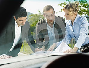Team Of Business People Signing Contract On Car Hood