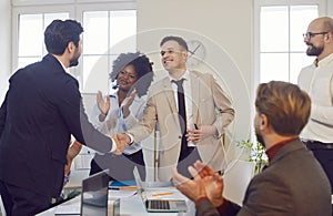 Team of business professionals applauding after successful handshake between two colleagues.