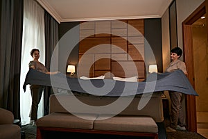 Team of chambermaids occupied with bed-making in hotel room
