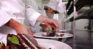 Team of chefs garnishing dessert plates with mint leaves and strawberries