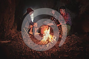 Team of climbers man and woman hiker camping.They are sitting around fire camp in the cave.