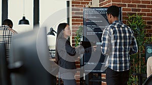 Team of coders analyzing code on wall screen tv comparing errors using digital tablet