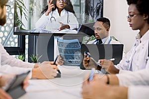 Team of confident multiethnic doctors having video conference meeting in modern hospital room. Group of professional