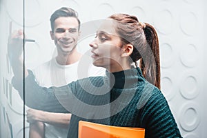 Team of coworkers brainstorming business strategy standing at office space behind glass wall with sticky notes