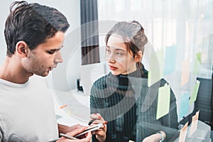 Team of coworkers brainstorming business strategy standing at office space behind glass wall with sticky notes