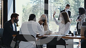 Team of diverse young happy business people working at modern office table wearing masks. Safety measures at workplace.