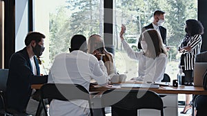 Team of diverse young happy business people working at modern office table wearing masks. Safety measures at workplace.