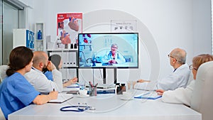 Team of doctors having video conference sitting at desk in hospital meeting room