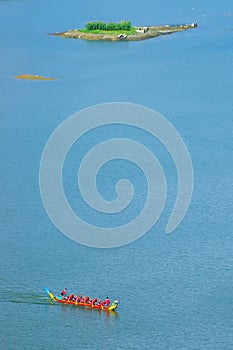 A team of dragon boats crosses the lake on a sunny day and the colors of the boats contrast with the clear blue water