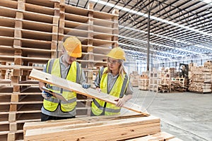 Team engineer carpenter wearing safety uniform and hard hat working holding clipboard checking quality of wooden products at