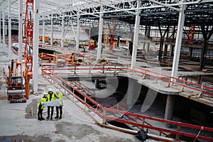 Team of engineers and construction workers reviewing blueprints, building site.