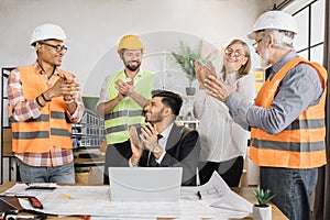 Team of engineers rejoices clapping their hands looking at laptop after a successful project.