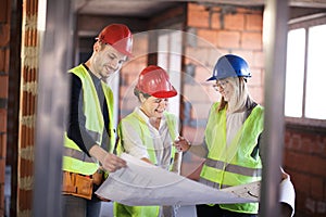 Team of engineers in vests and hard hats with schematics on a construction site photo