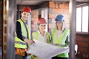 Team of engineers in vests and hard hats with schematics on a construction site