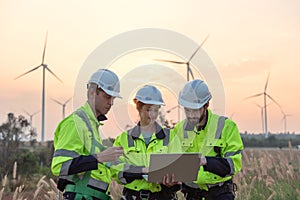 Team of engineers working and using a computer laptop on site in wind turbine farm, Wind turbines generate clean energy source,