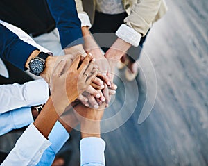 In a team, everybody wins. a group of unrecognisable businesspeople joining their hands together in unity in an office.