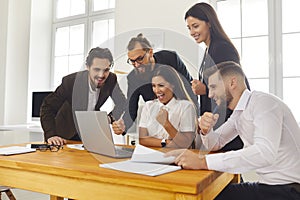 Team of excited colleagues looking at laptop screen celebrating successful sales