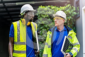 Team factory worker technician engineer men in green working suit dress and safety helmet talking and holding solar panel.