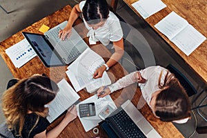 Team of female accountants preparing annual financial report working with papers using laptops sitting at desk in office