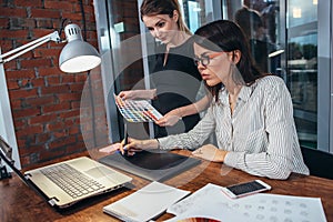 Team of female interior designer drawing a new project using graphic tablet, laptop and color palette sitting at desk in