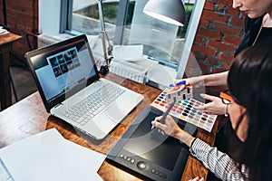 Team of female interior designer drawing a new project using graphic tablet, laptop and color palette sitting at desk in