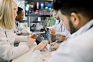 Team of five diverse multiethnic doctors having video conference meeting in hospital, chatting with their two young