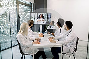 Team of five multiethnical doctors having video conference meeting in hospital with their young African woman doctor