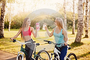 Team of girls bike with bottle of water in park on sunset background