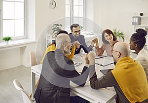 Team of happy business people sitting around an office table, holding hands and smiling