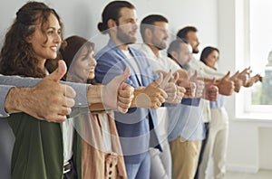 Team of happy business people standing in row and showing thumbs up gesture all together