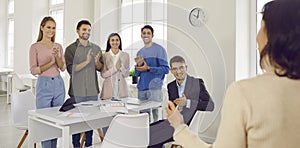 Team of happy young business people applauding speaker during work meeting in office