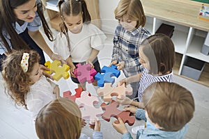 Team of little children together with their teacher join pieces of a jigsaw puzzle