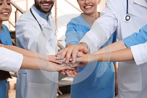 Team of medical doctors putting hands together indoors. Unity concept