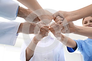 Team of medical doctors putting hands together on light background. Unity concept