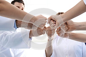 Team of medical doctors putting hands together on light background. Unity concept