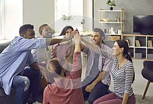 Team of multinational friends raises their hands during a meeting at home and folds them together.