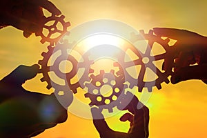 Team of people with gears in hands on sunset background.