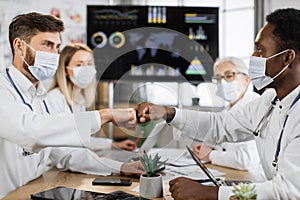 Team of physicians in face masks giving fist bump indoor