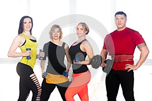 Team of positive sporty people posing with dumbbells in gym