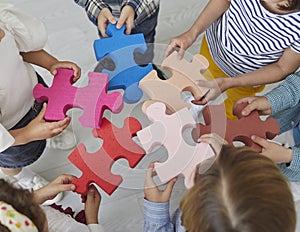 Team of school kids standing in the classroom and joining pieces of a jigsaw puzzle