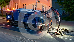A team of road builders perform road repairs at night with the help of a large truck vacuum cleaner. Professional repairmen change photo