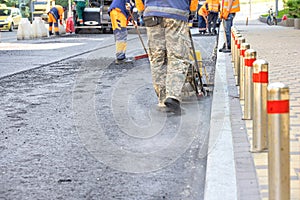 A team of road service workers lays fresh asphalt at a road construction site