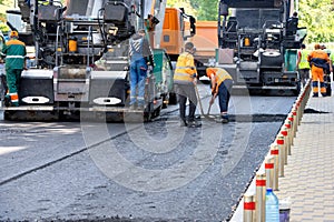 A team of road workers with asphalt pavers lay down fresh asphalt on a city street on a summer day