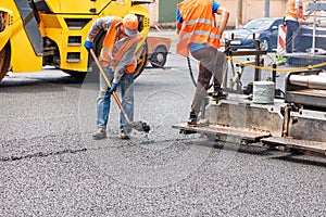 A team of road workers is laying fresh asphalt with industrial road machinery