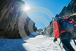 Team roping up woman dressed high altitude mountaineering clothes and harness climbing with backpack by snowy slope in the couloir