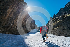 Team roping up woman dressed high altitude mountaineering clothes and harness climbing with backpack by snowy slope in the couloir