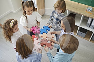 Team of school children standing in classroom and joining pieces of jigsaw puzzle