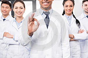 Team of smiling professional doctors standing together while their leader is showing ok