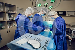 A team of surgeons in a blue uniform operates on a patient in a hospital. Side view of young doctors at work